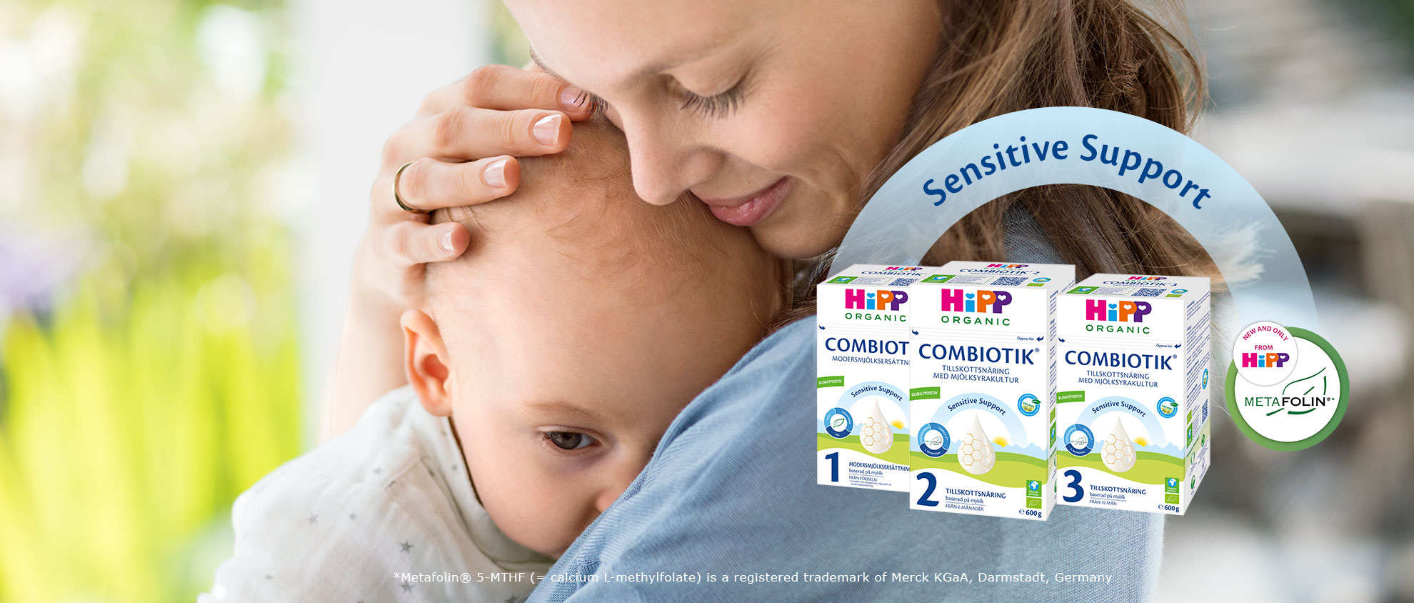 En kvinna håller kärleksfullt om en bebis, med en produktförpackning med "Sensitive Support" och "Metafolin" i bakgrunden.
