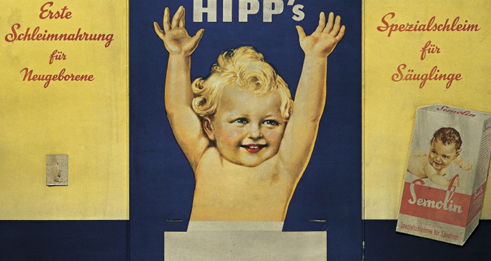 Vintageannons med en glad bebis med armarna i vädret, omgiven av text på tyska, som marknadsför en produkt som heter "HIPP's" och "Semolin".